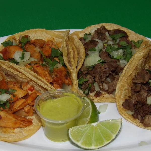 Four tacos, two chicken and two beef, with cilantro, onions, lime, and green sauce.