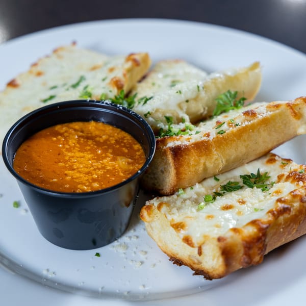 Cheesy garlic breadsticks with parsley and a side of red marinara sauce on a white plate.
