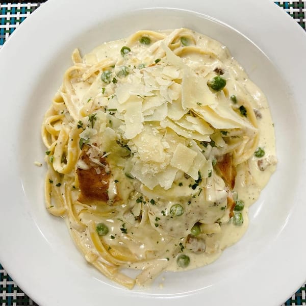 Creamy fettuccine Alfredo with peas, chicken, and shaved Parmesan cheese in a white bowl.