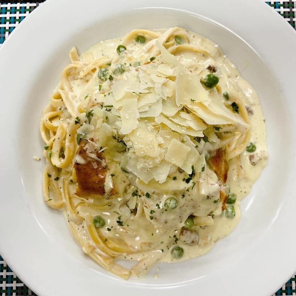 Creamy fettuccine Alfredo with peas, chicken, and shaved Parmesan cheese in a white bowl.