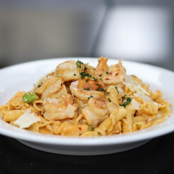 Pasta To Go's creamy shrimp pasta with penne, parmesan, and parsley in a white bowl.