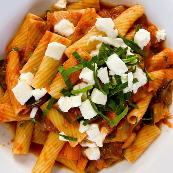 Rigatoni pasta with red sauce, mozzarella, and basil in a white bowl from Pasta To Go.