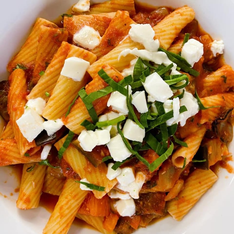 Rigatoni pasta with red sauce, mozzarella, and basil in a white bowl from Pasta To Go.